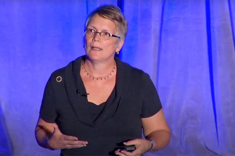 woman on stage speaking wearing glasses with short hair