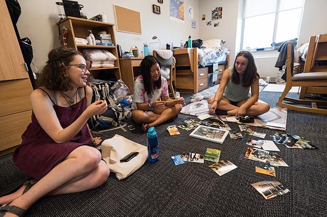 Three students sitting on the floor in a dorm room.