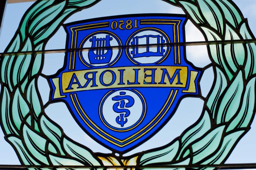 The University of Rochester's Meliora logo and shield insignia in stained glass